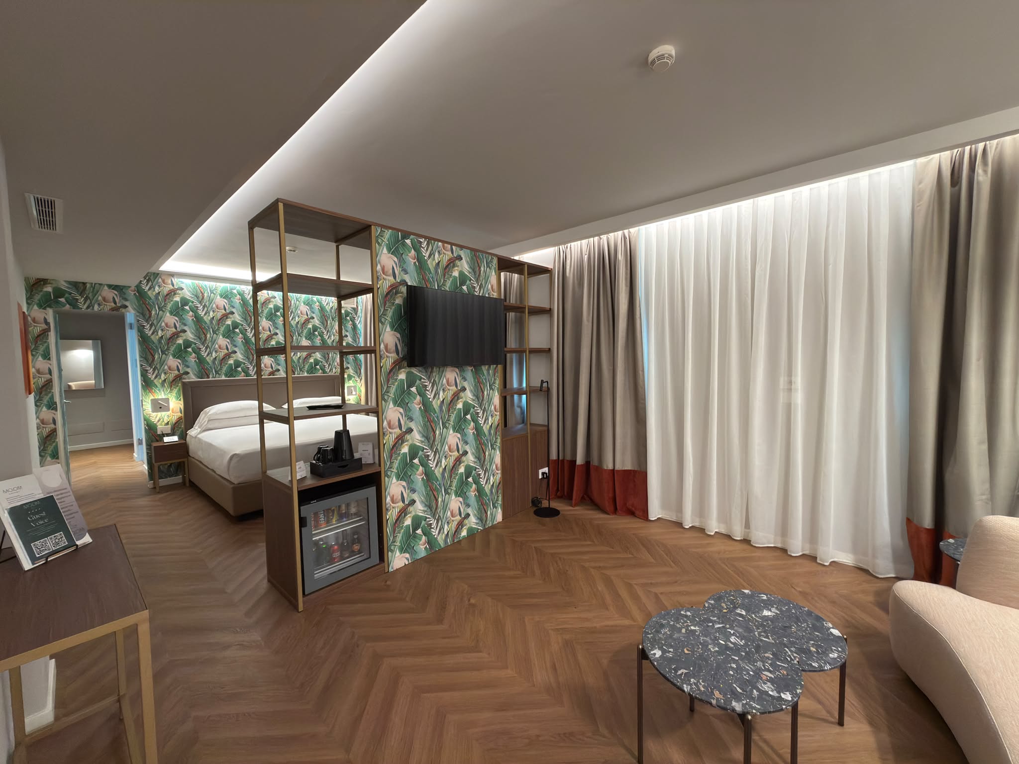 Superior Suite with a wooden double bed, partition cabinet with integrated desk, large wall mirror, wall-mounted TV, and spacious windows with white curtains