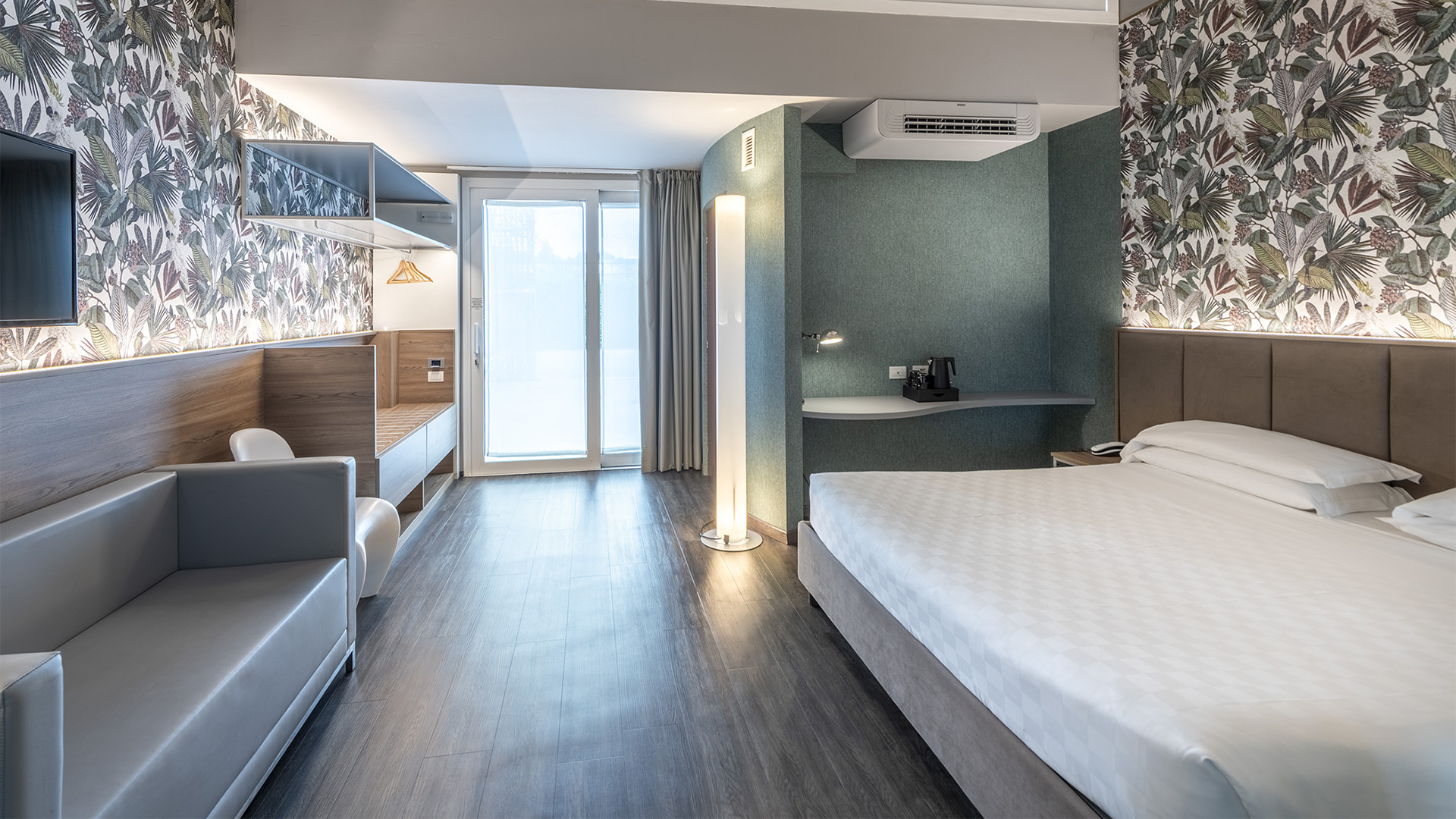 Luxurious Deluxe suite with soft lighting, grey sofa, bed, green leaf wallpaper, and grey curtains