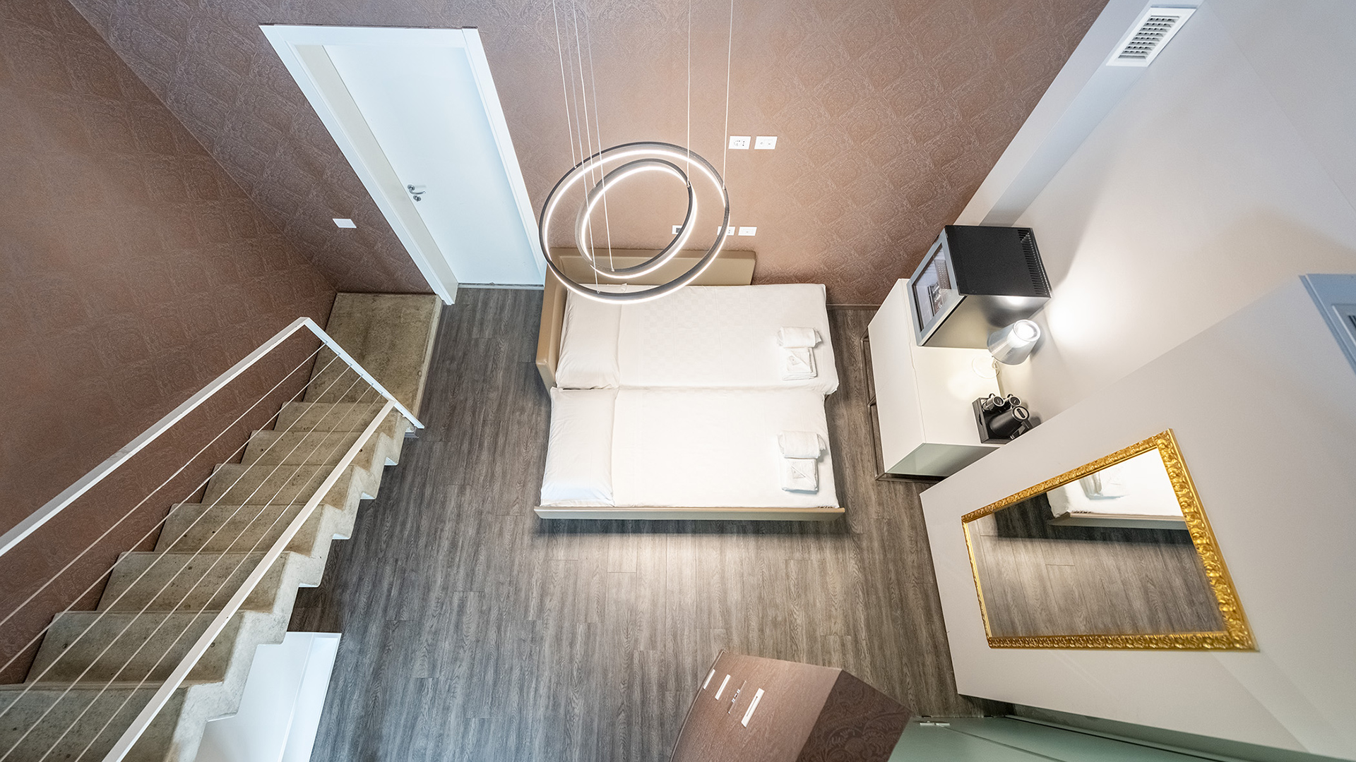 Elegant room of the MO.OM Hotel with two beds, brown walls, wooden floor, and golden details