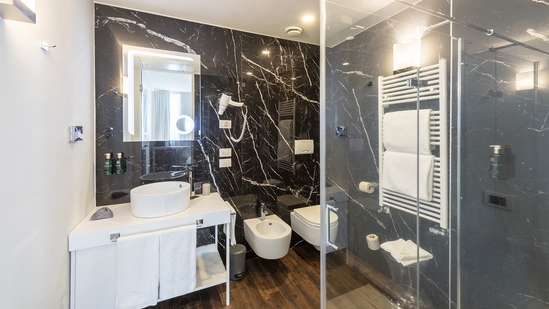 Elegant superior room bathroom: polished black marble, white furniture, and clear glass shower